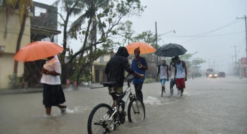 Haitian people travel in a flooded street through the rain, during a tropical storm in the commune of Les Cayes, Haiti, on October 21, 2016