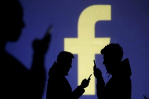 FILE PHOTO: Silhouettes of mobile users are seen next to a screen projection of Facebook logo in thi