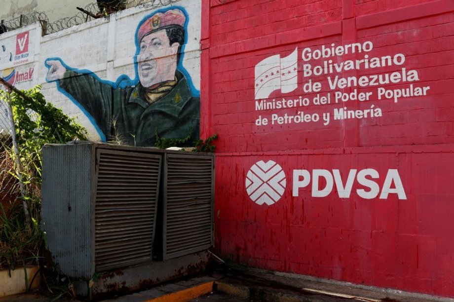 The logo of Venezuelan state oil company PDVSA next to a mural depicting late Venezuelan President Hugo Chavez at a gas station in Caracas, March 2, 2017.