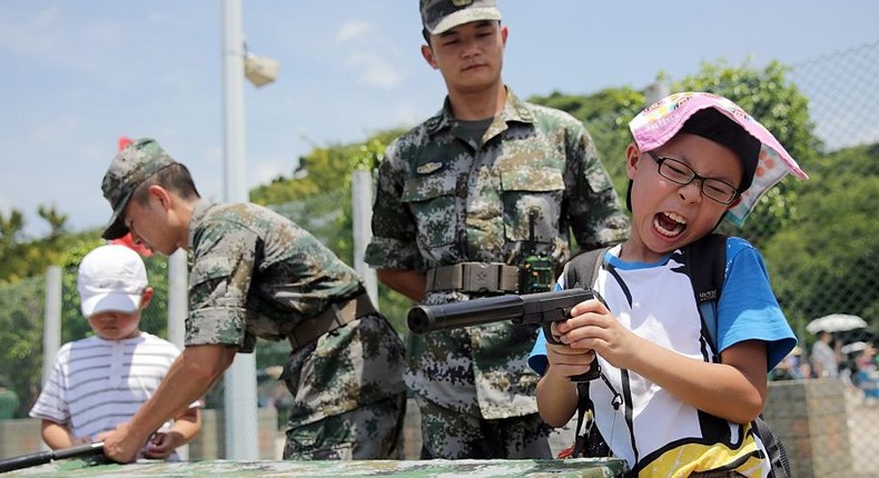 A child reacts as he pretends to use a handgun while under guidance by a Peoples' Liberation Army (PLA) soldier at the Ngong Shuen Chau Barracks in Hong Kong on July 1, 2015.