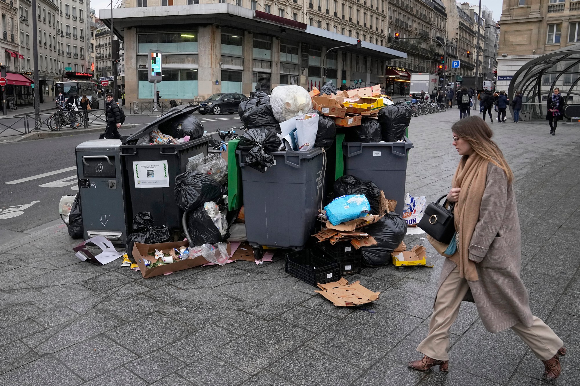 Žena kráča okolo preplnených smetných košov v Paríži v utorok 7. marca 2021. 