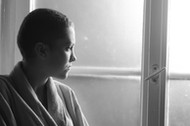 Young depressed cancer patient standing in front of hospital window