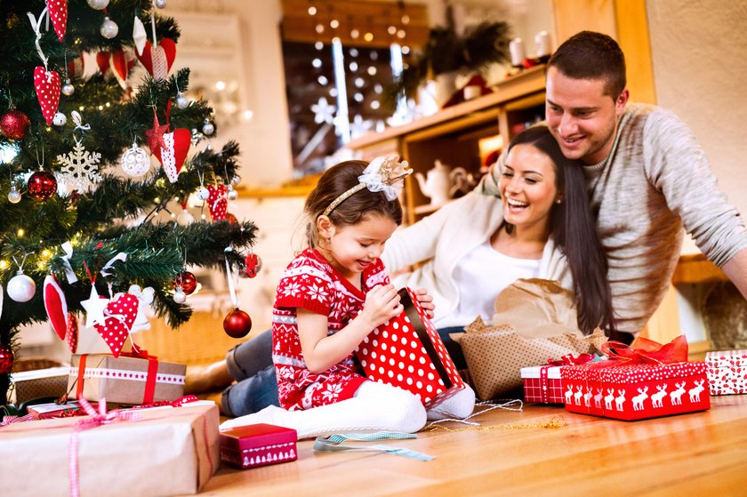 Young family with daughter at Christmas tree at home.