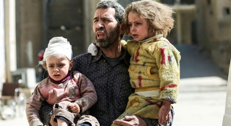 A Syrian man carries two injured children after a reported air strike in the rebel-controlled town of Hammuriyeh, on the outskirts of the capital Damascus, on March 25, 2017