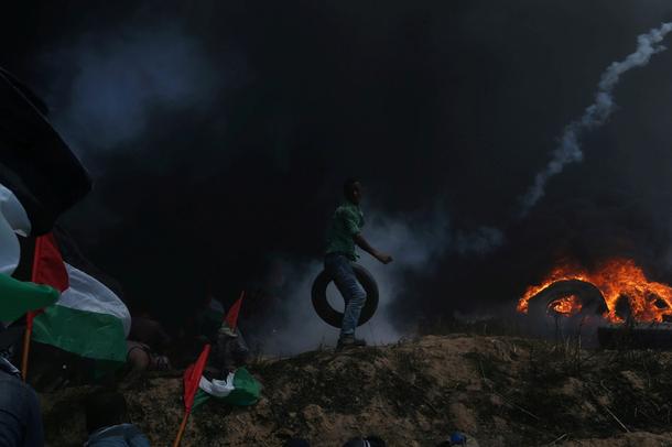 Palestinian demonstrator carries a tire as others take cover from Israeli fire and tear gas during a