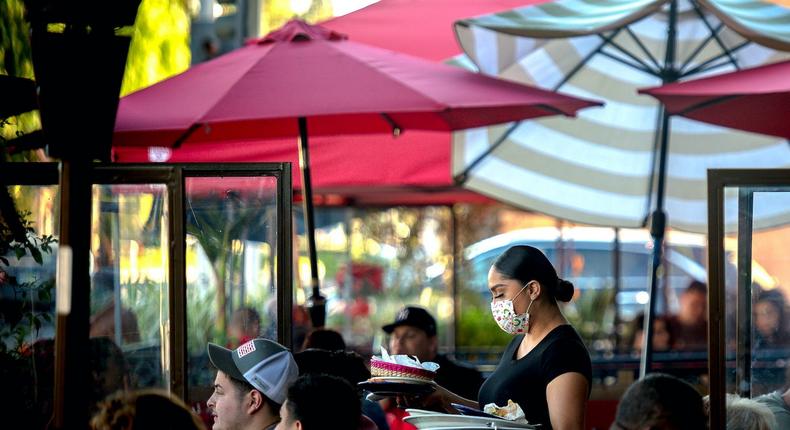 A server clears a table as patrons dine outdoors at Gloria's Cocina Mexicana restaurant in California on Saturday, Dec. 5, 2020.
