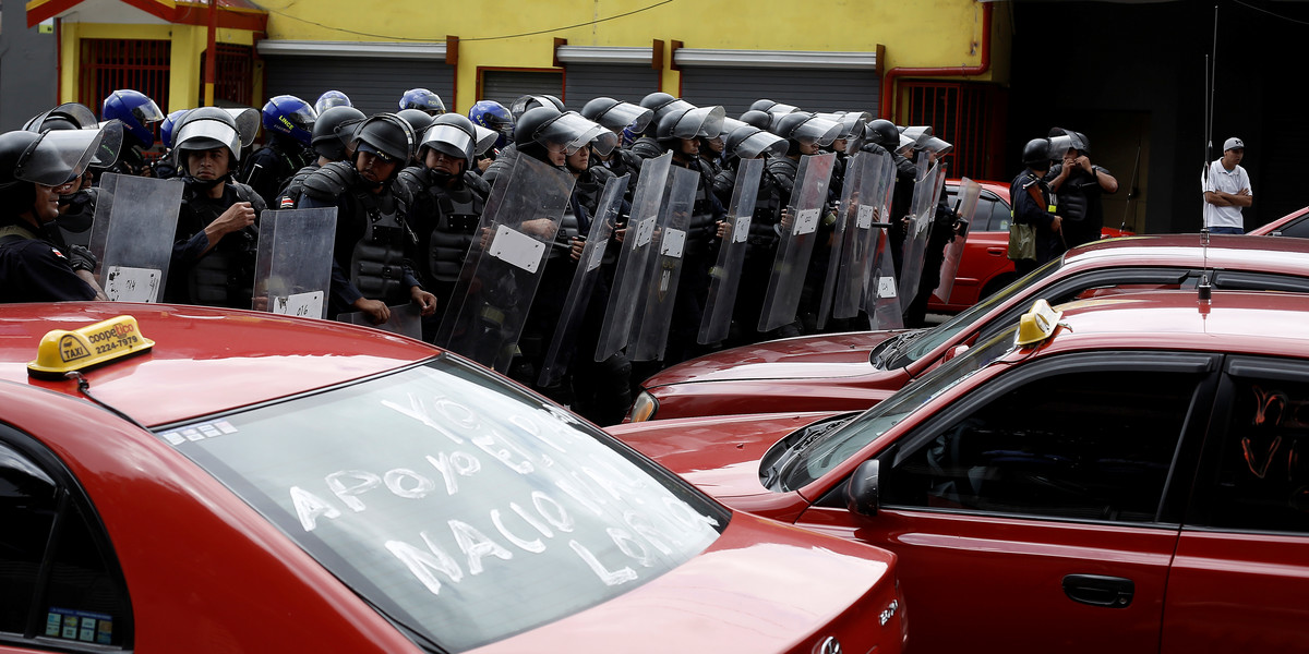 Riot police stand near taxi drivers blocking a highway during a protest against ride-hailing service Uber in San Jose, Costa Rica, August 9, 2016.