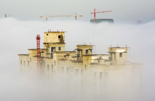 Cranes and residential buildings under construction are seen among thick fog in Anyang