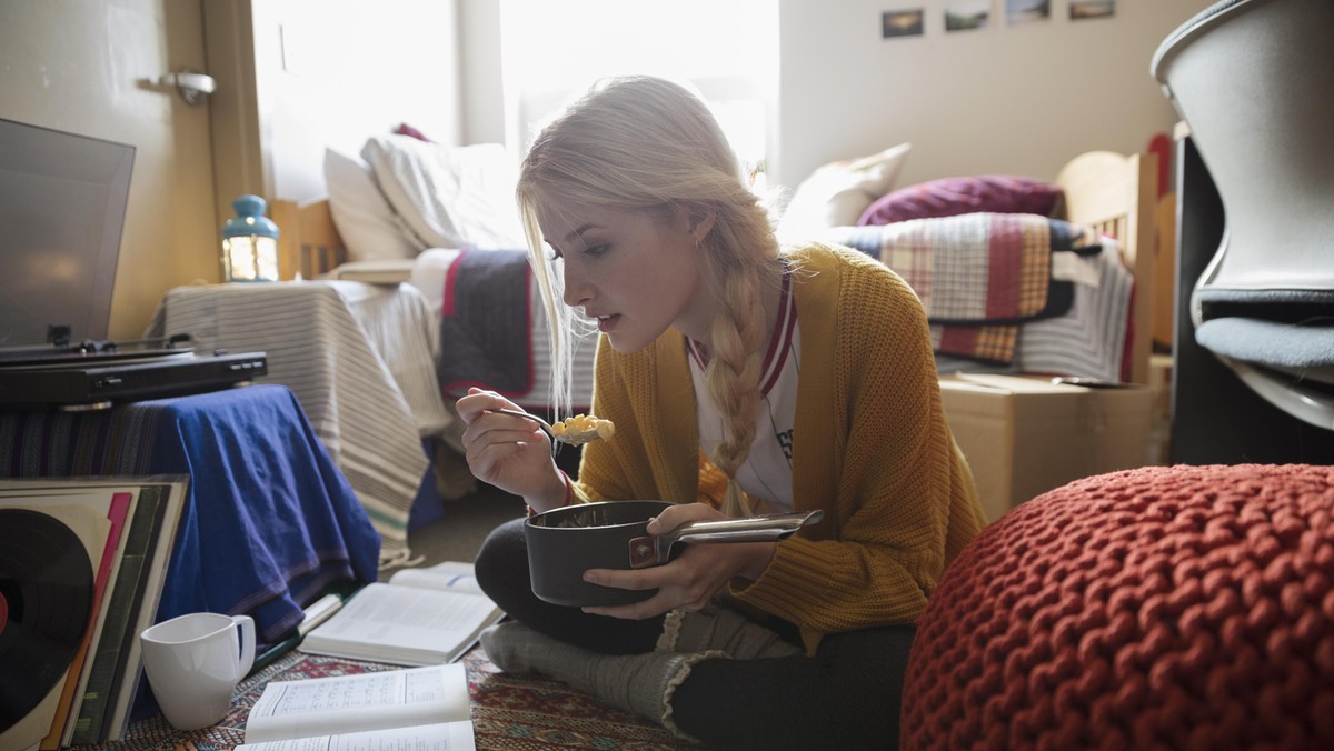 Female college student eating and studying on floor in dorm room