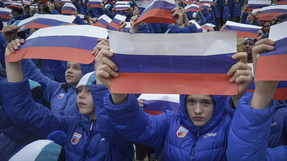 Dzieci trzymają rosyjskie flagi podczas propagandowych uroczystości w rocznicę pseudoreferendum na Krymie