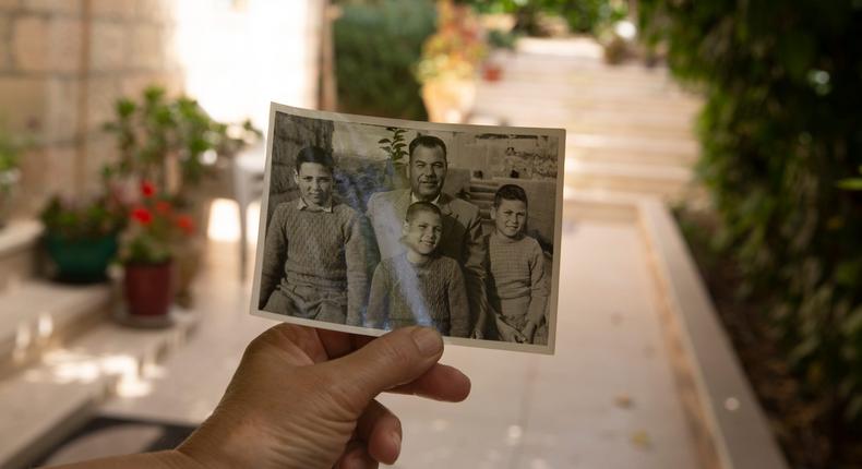 Samira Dajani holds a photo of her father, Fouad Moussa Dajani and his sons, taken in the same place in the courtyard of their home in the Sheikh Jarrah neighborhood of east Jerusalem, Sunday, May 9, 2021. When Samira Dajani's family moved into their first real home in 1956 after years as refugees, her father planted trees in the garden, naming them for each of his six children.
