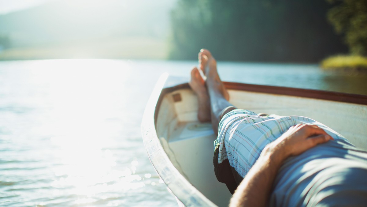 Man laying in rowboat on tranquil lake