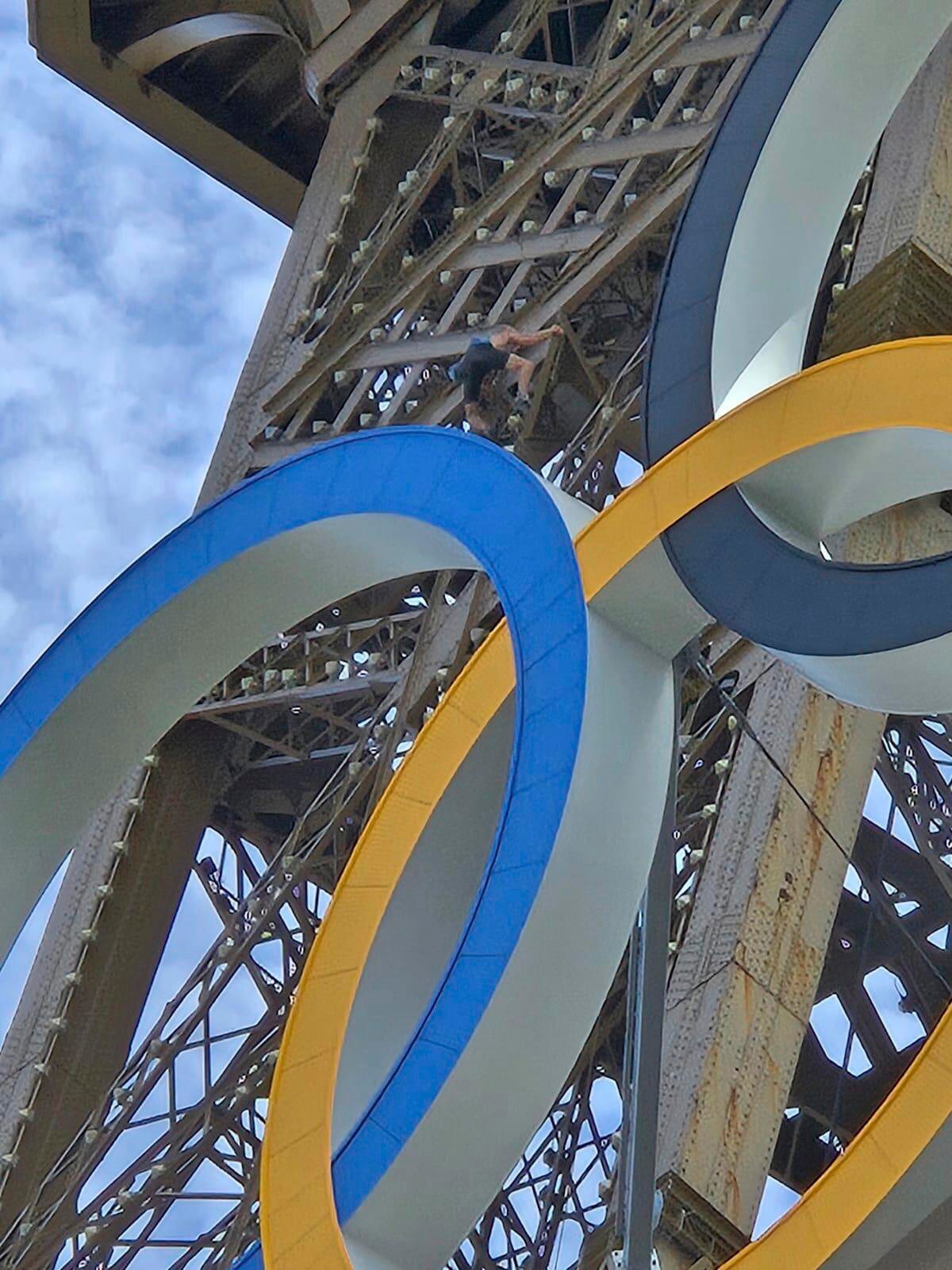 Muž lezie na Eiffelovu vežu počas OH 2024 v Paríži.