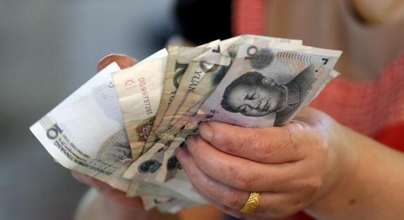 A vendor holds Chinese Yuan notes at a market in Beijing, August 12, 2015. REUTERS/Jason Lee