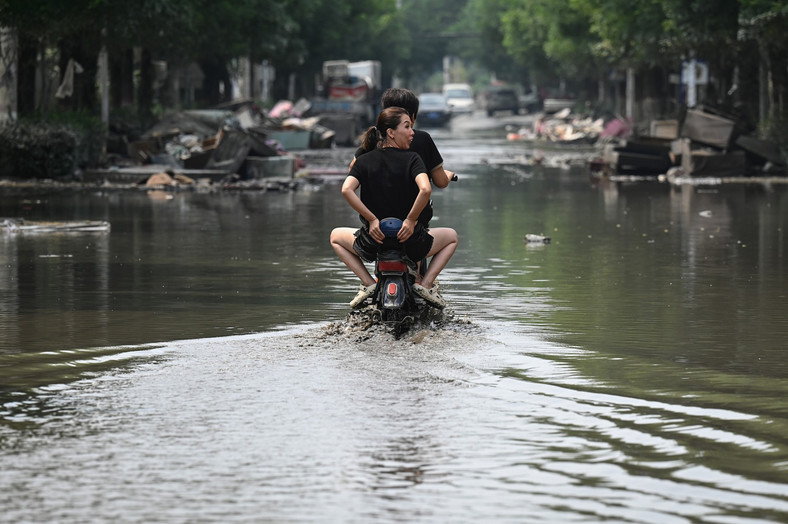 Mieszkańcy jeżdżą skuterem po zalanej ulicy w następstwie powodzi spowodowanej ulewnymi deszczami w mieście Zhuozhou w północnochińskiej prowincji Hebei w dniu 9 sierpnia 2023 r.