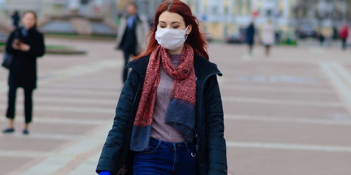 Young female using a face mask as a coronavirus spreading prevention walking with her dog. Global CO