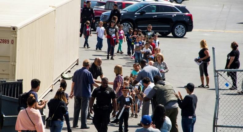 A police officer leads children to be reunited with parents after a gunman entered a classroom and killed one woman and one student, before turning the gun on himself, at North Park Elementary School in San Bernardino, California