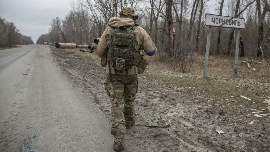 Ukraiński żołnierz przechodzi obok znaku drogowego na końcu obszaru zabudowanego z napisem "Czarnobyl"