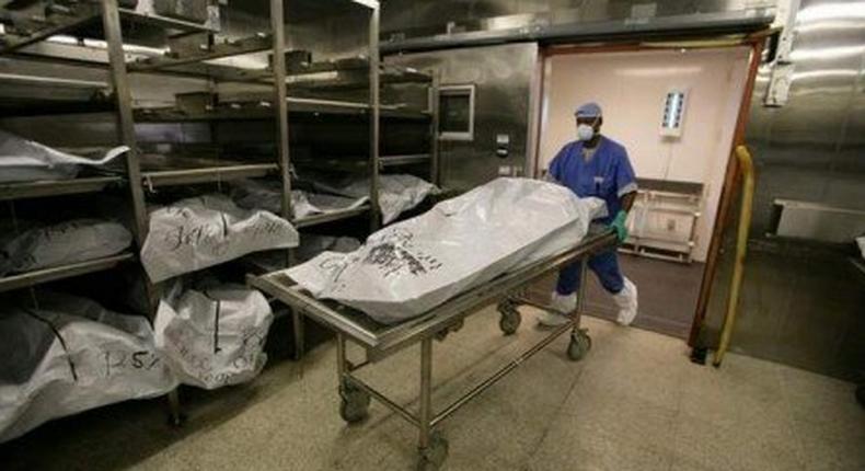Morgue attendant is seen pushing a corpse lying on a gurney,