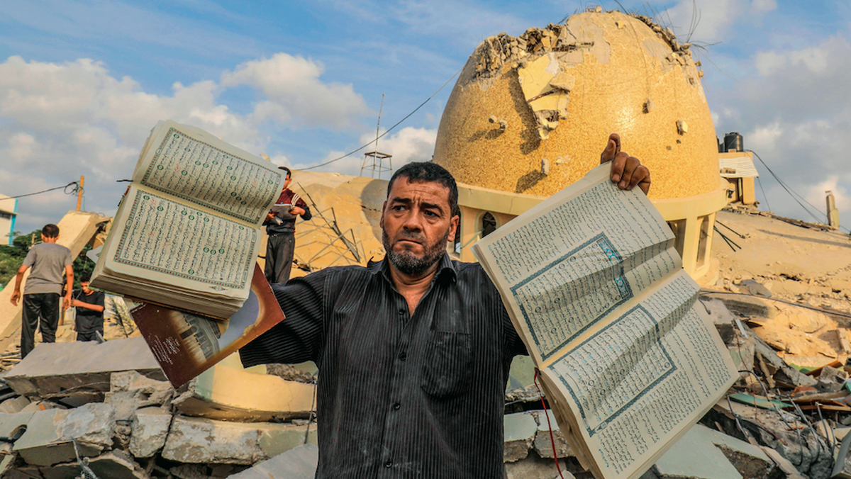 A man holds books of the Quran in front of a mosque destroyed by Israeli airstrikes.