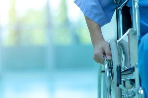 Asian disabled man is sitting in a wheelchair. He holds his hands on the wheel. Nearby are his colleagues, Medical equipment.