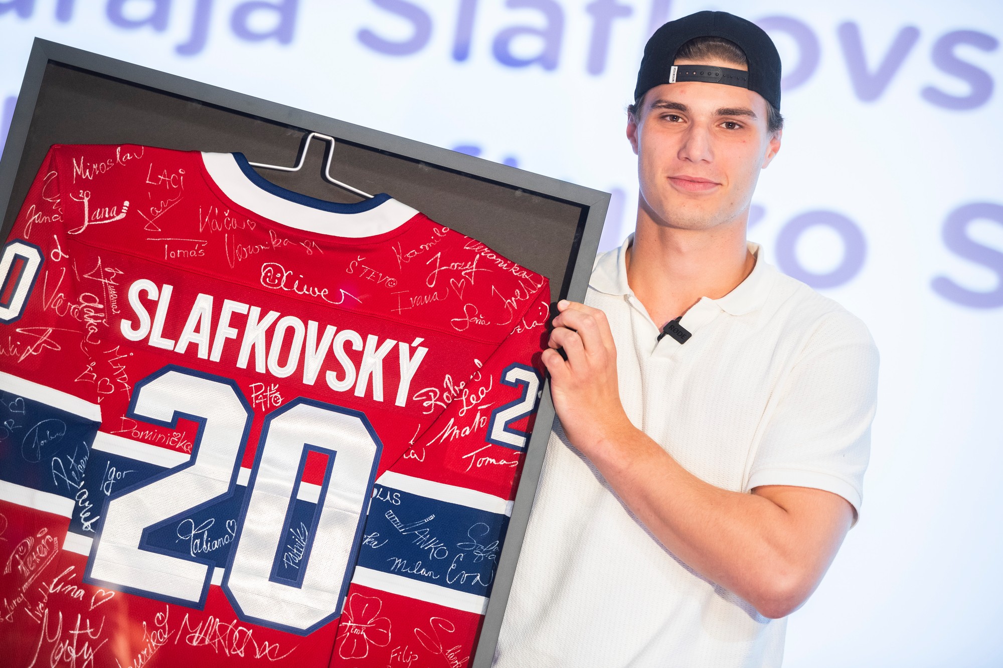 Slovenský hokejista Juraj Slafkovský pózuje so svojím dresom s číslom 20 podpísanom fanúšikmi.