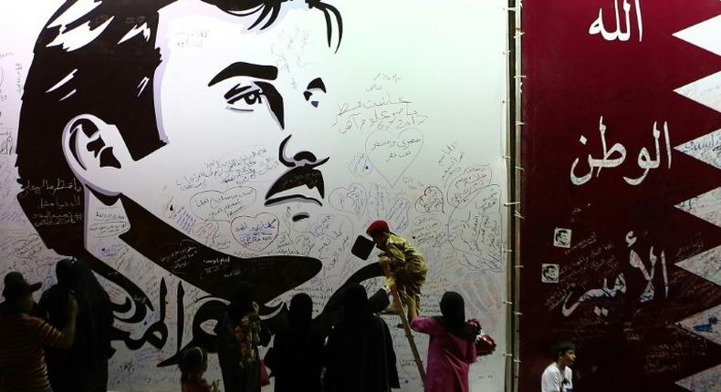 Qataris write comments on a wall bearing a portrait of Qatar's Emir, Sheikh Tamim bin Hamad Al Thani, which has become the symbol of Qatari resistance during the row between Doha and neighbouring countries, in Doha on July 6, 2017