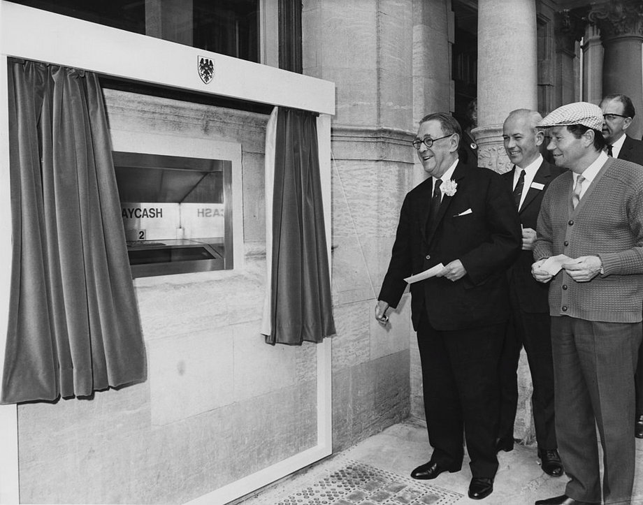 Pierwszy bankomat na świecie w Barclays Bank. Na pierwszym planie prezes sir Thomas Bland i aktor Reg Varney - obaj z papierowymi kartami służącymi do wypłaty pieniędzy
