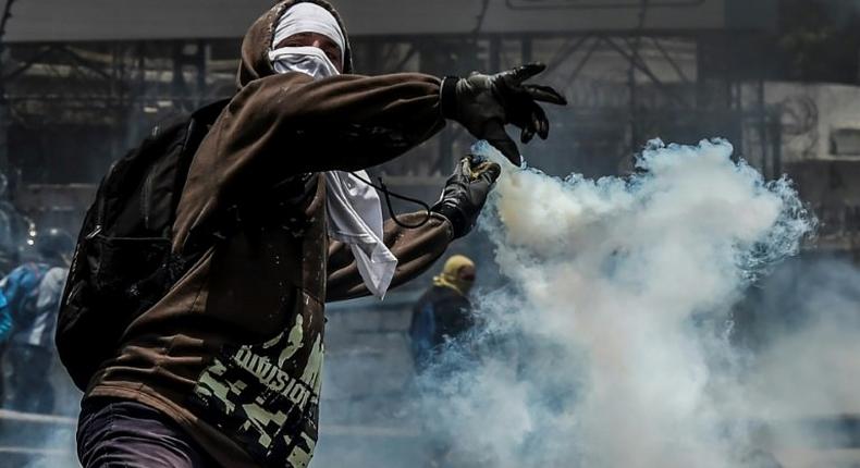 A demonstrator protesting against President Nicolas Maduro's government throws back a tear gas grenade at riot police, in Caracas, on April 10, 2017