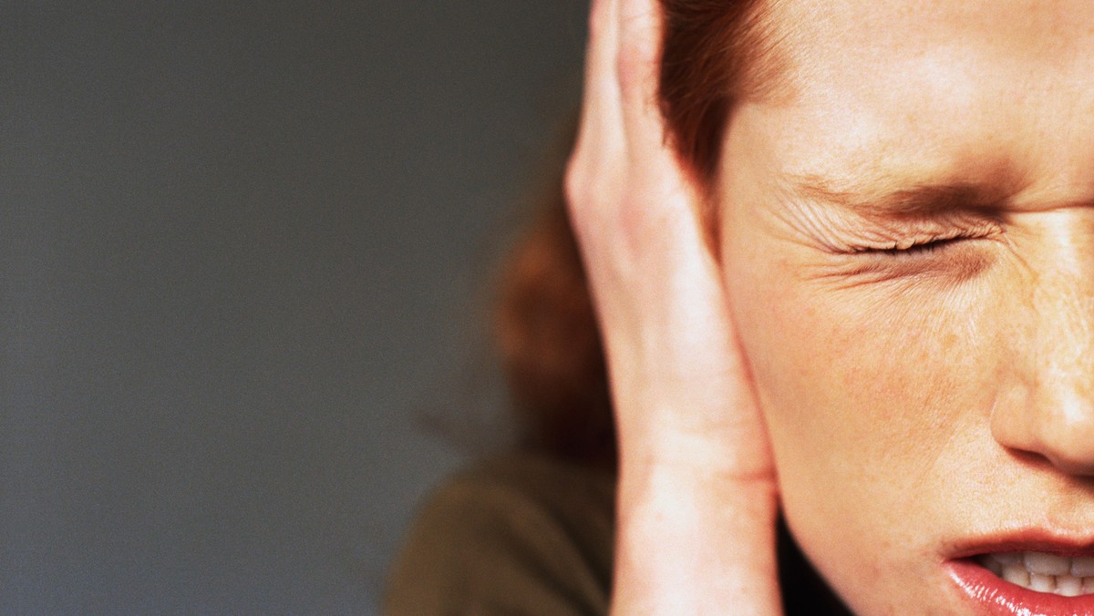 Young woman squinting eye closed, hand covering ear, close-up