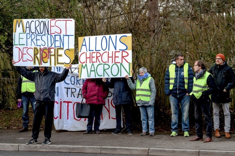 Demonstrators hold placards reading "Macron is the president of the rich" and "Let's go get Macron" during a visit to a tax centre in the northern French city of Amiens by the budget minister