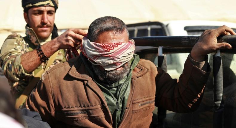 A suspected Islamic State (IS) group fighter who fled from the frontline Syrian village of Baghouz, near the Iraqi border, sits blindfolded in the back of a pickup truck after he was taken into custody by SDF forces for screening