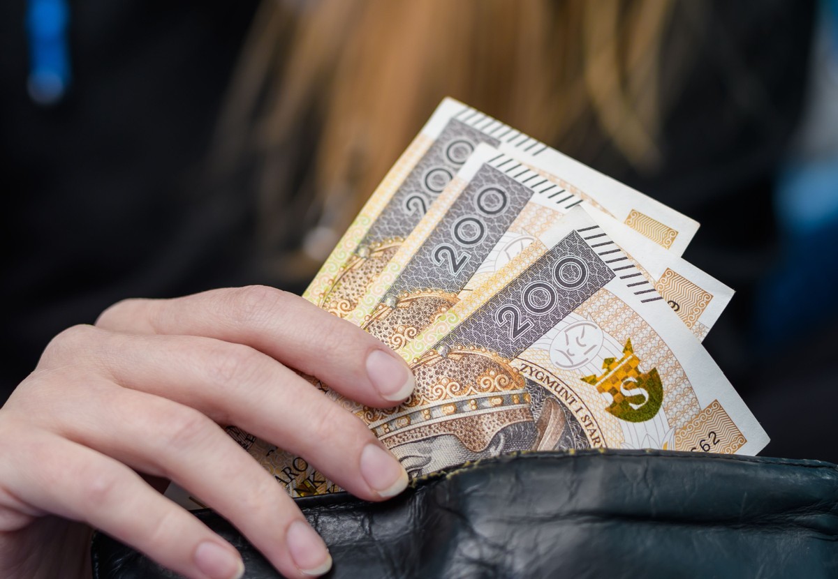 Osoba trzymająca w dłoni banknoty 200 zł wyciągnięte z portfela.