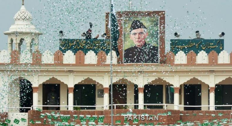 The portrait of Muhammad Ali Jinnah is seen at the India-Pakistan Wagah border post as a Pakistani Ranger (top) unfurls the national flag on Independence Day