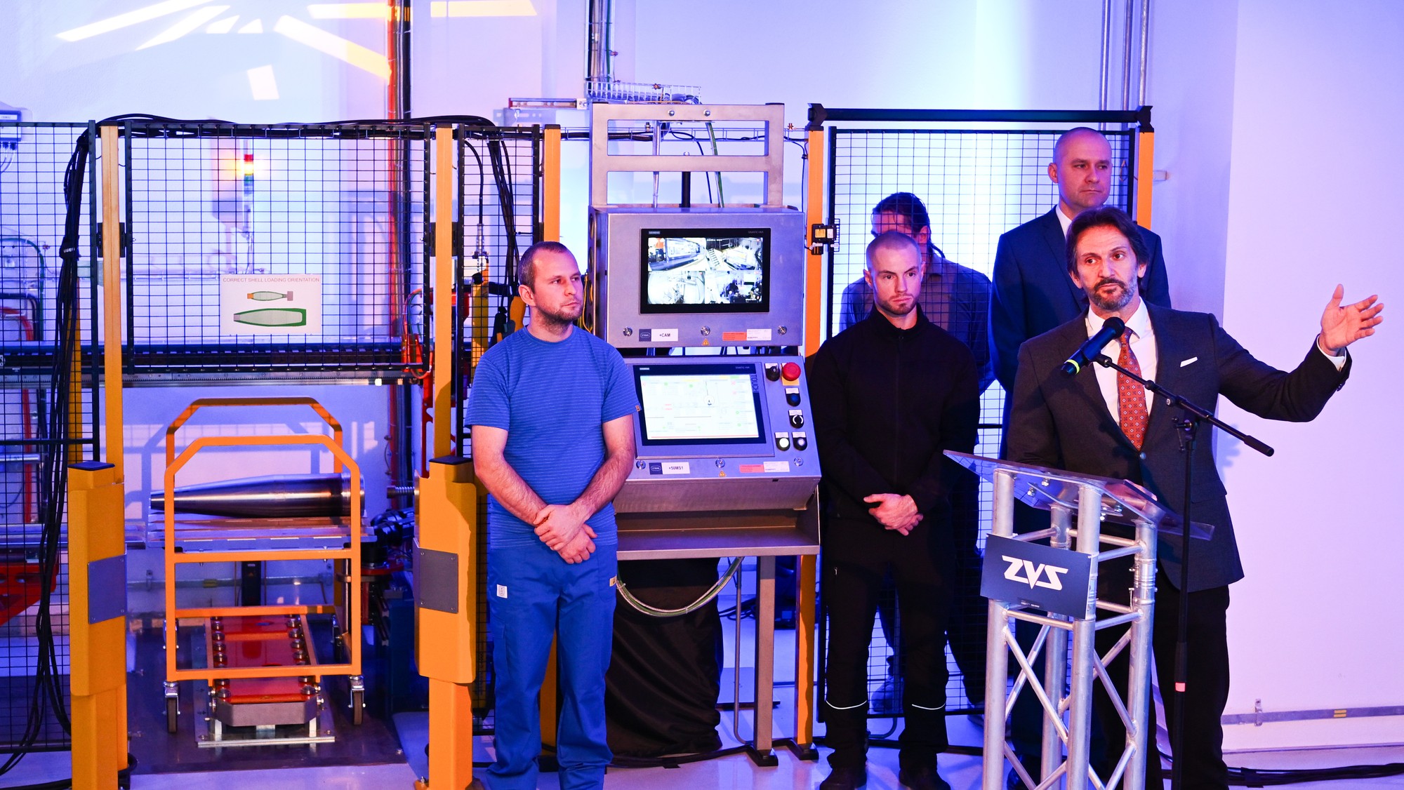 Na snímke sprava minister obrany Slovenskej republiky Robert Kaliňák (SMER - SD) a vľavo operátori výroby počas slávnostného spustenia do prevádzky novej automatizovanej linky na plnenie tiel munície 155 mm v závode ZVS Holding v Dubnici nad Váhom v utorok 16. decembra 2025. FOTO TASR - Martin Medňanský