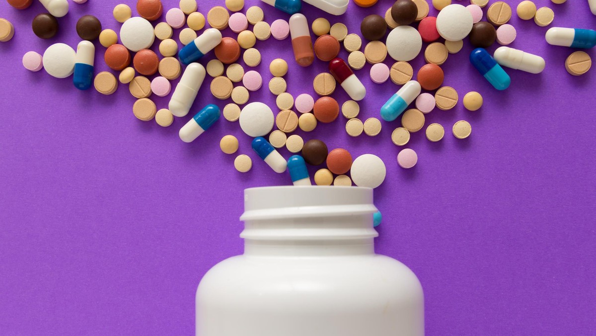 Capsules spilling out of white bottle. Violet background.