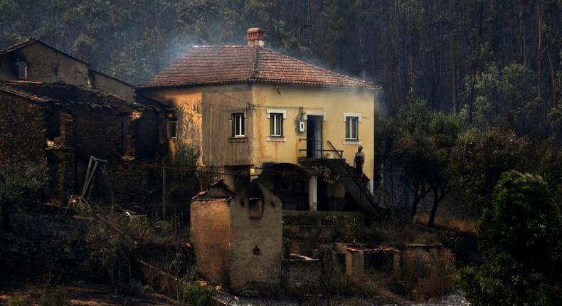 A man stands in the stairway of a house with smoke billowing from the roof in an area devastated by a wildfire in Canical, near Alvares, on May 18, 2017