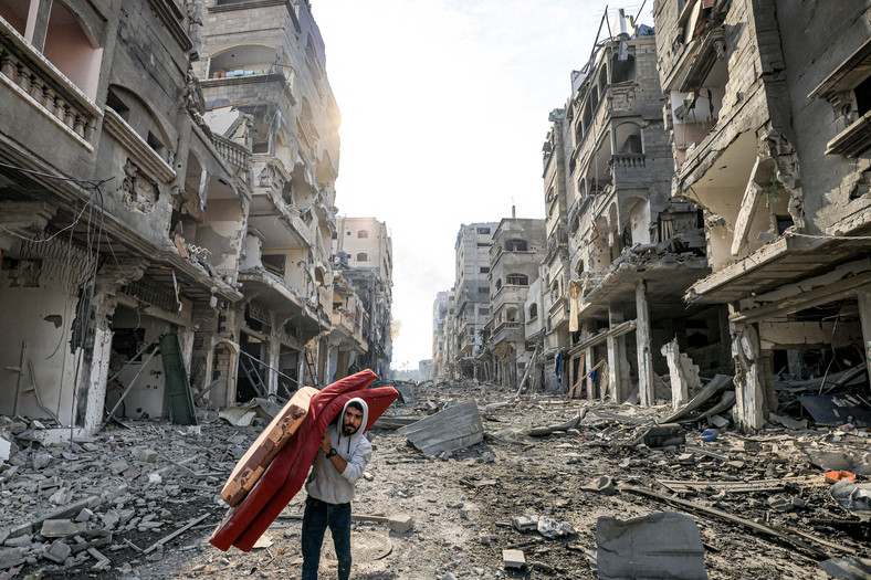 Mężczyzna idący przez zbombardowane osiedla w Strefie Gazy