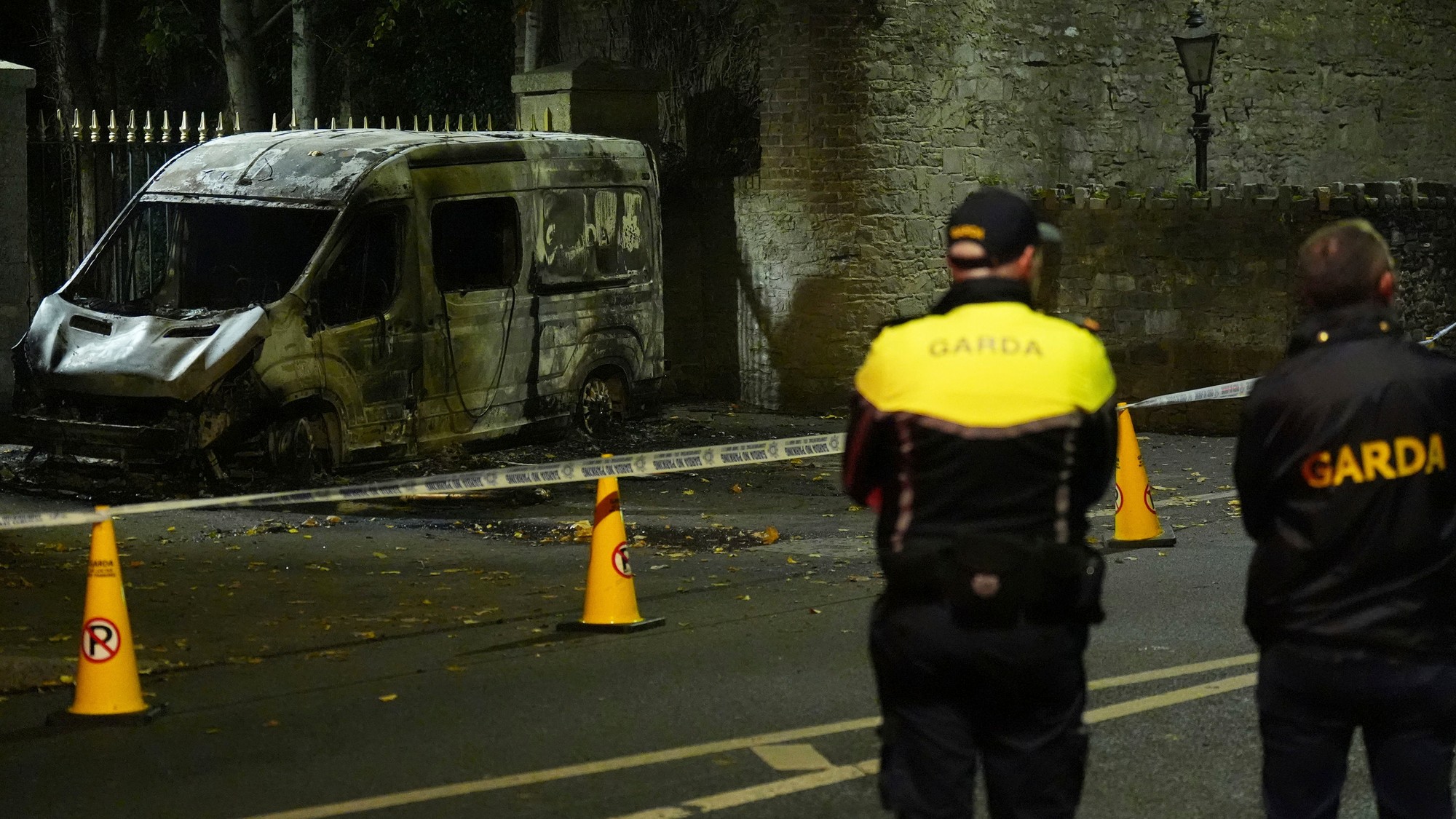 Policajti stoja pri vyhorenom policajnom vozidle v blízkosti miesta, kde došlo k nepokojom pred dublinským hotelom, v ktorom bývali žiadatelia o azyl.
