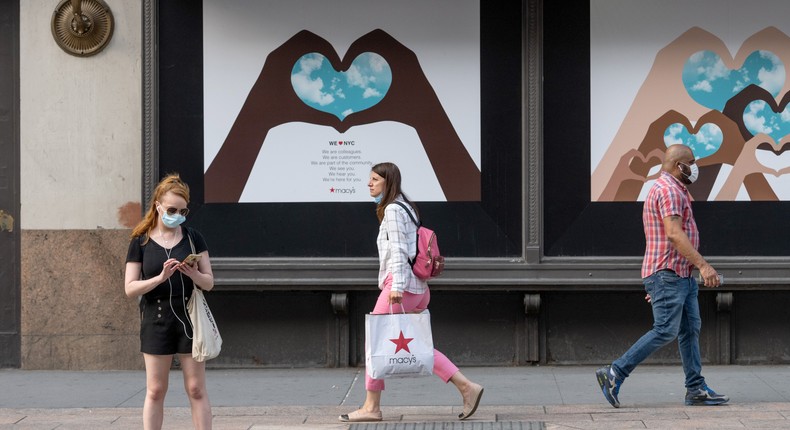 People with and without masks walk in front of artwork depicting hearts made by hands on the Macy's Store windows in Herald Square as the city moves into Phase 3 of re-opening following restrictions imposed to curb the coronavirus pandemic on July 7, 2020 in New York City.