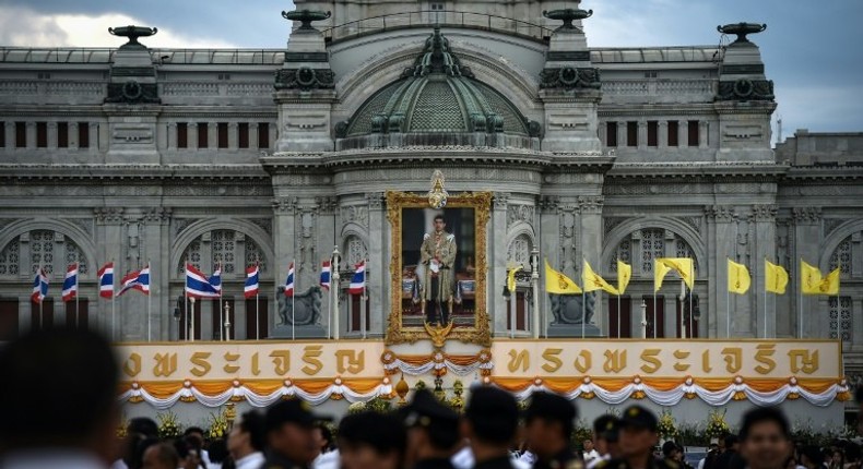 People gather before giving alms to Buddhist monks in front of a photograph of Thai King Maha Vajiralongkorn at the Royal Plaza in Bangkok on July 28, 2017