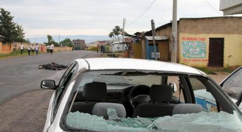 A car damaged by gunfire is seen abandoned as residents walk past bodies of unidentified men killed during gunfire, in the Nyakabiga neighbourhood of Burundis capital Bujumbura, December 12, 2015.