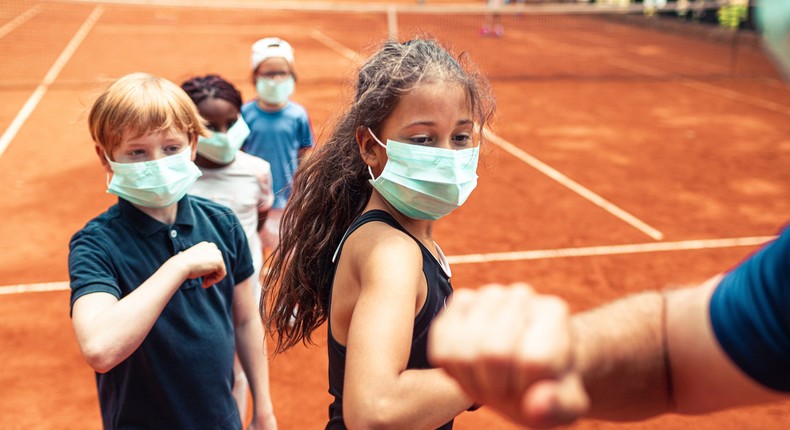 A group of kids elbow-bumping their tennis instructor after practice.
