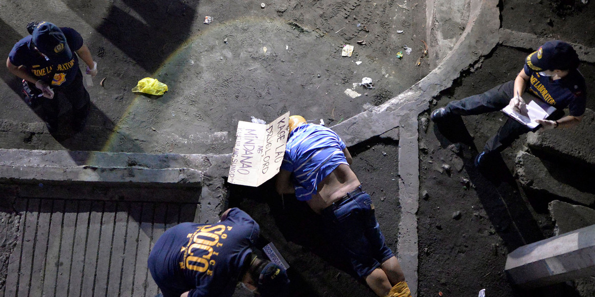 Police officers inspect the body of a man who police said was a victim of a drug-related vigilante execution in Manila. The cardboard found near his body reads: "Kage Lao, drug lord from Mindanao. You are next."