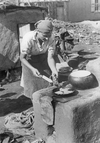 Na zdjęciu kobieta przygotowująca posiłek pod gołym niebem, sierpień 1942 roku