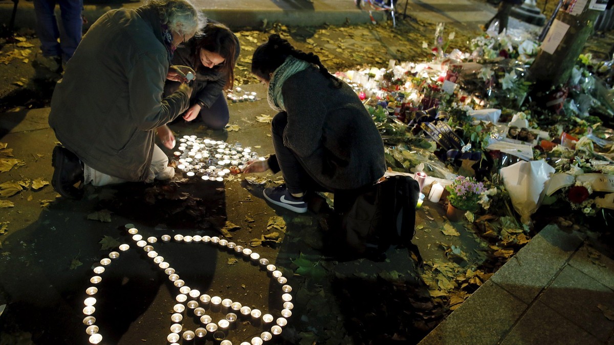 People kneel as they light candles to pay tribute to victims near the site of the attack at the Bata