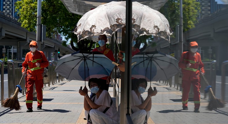 Residents cover up from the sun with umbrellas as they wait for a bus in Beijing, on July 15, 2022.