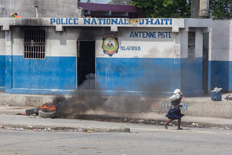 Kobieta przemyka ulicą, w tle widać płonące opony i podpalony komisariat. Wcześniej uzbrojeni gangsterzy ostrzeliwali się z policją i żołnierzami na terenie lotniska w Port-au-Prince
