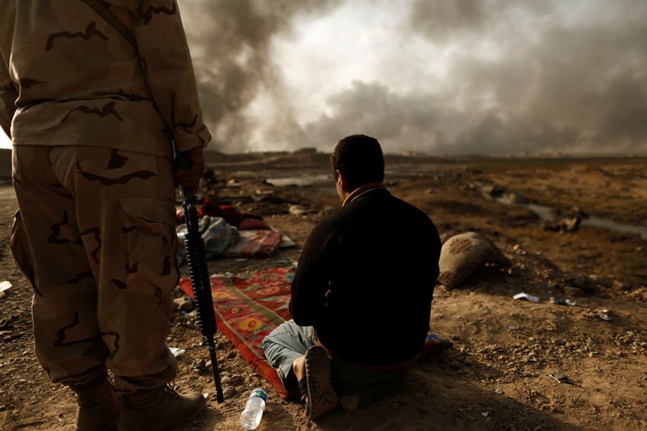 An Iraqi soldier stands next to a detained man accused of being an Islamic State fighter, at a check point in Qayyara, northern Iraq, October 30, 2016.