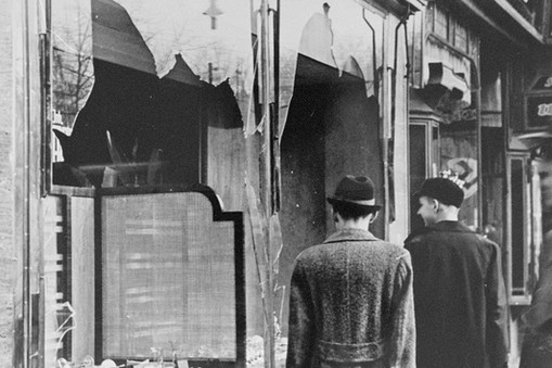 Germans pass by the smashed windows of a Jewish-owned shop. The aftermath of Kristallnacht (Night of